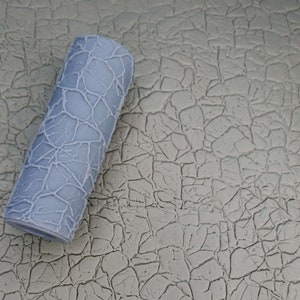 May include: A gray textured paint roller with a cracked pattern design. The roller is lying on a gray textured surface.