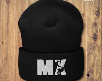 May include: Black beanie with a white embroidered "MX" design, featuring a motorcycle silhouette. The beanie has a folded cuff and is made of a soft, knitted material. The text "A-BUDDIES SHOP" is in the upper right corner.