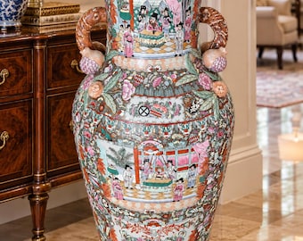 May include: A large, floor-standing porcelain vase featuring a flared rim and two sculpted handles shaped like coiled dragons. The exterior is decorated with intricate, colorful scenes of figures in traditional attire, surrounded by floral patterns.