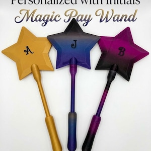 May include: Three star-shaped wands with personalized initials. The wands are gold, blue-purple, and purple-black, each with a matching handle. The text "Personalized with Initials Magic Pay Wand" is at the top.