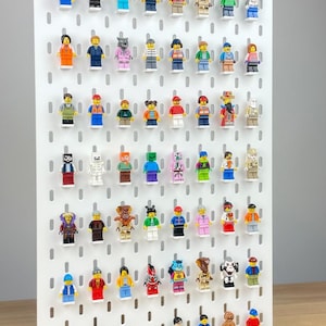 May include: A white pegboard display with numerous colorful Lego minifigures attached. The minifigures showcase a variety of characters with different outfits and accessories. The display is mounted on a wooden base.