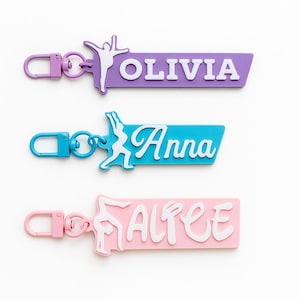 May include: Three personalised keychains in purple, blue, and pink. Each keychain features a gymnast silhouette and a name: Olivia, Anna, and Altee, in white. The keychains have matching coloured clasps.