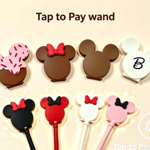 May include: A selection of Mickey Mouse-themed Tap to Pay wands in shades of brown, black, red, pink, and white. Some wands have a bow, and one has a letter "B". The top row shows the wand heads, while the bottom row shows the wands with handles.