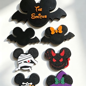 May include: A collection of seven black mouse-shaped magnets with Halloween designs, including a bat-winged version with the text The Smiths, a mummy, a red-eyed devil with a pitchfork, a skeleton, and a witch with a purple hat and green bow.