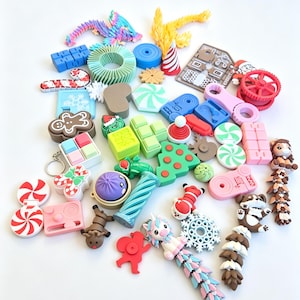 Puede incluir: Una colección de pequeños objetos de plástico impresos en 3D y coloridos, que incluye dragones articulados, un hombre de jengibre, una figura de Santa Claus, varias formas geométricas, copos de nieve, bastones de caramelo, un unicornio y renos.