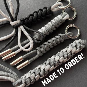 May include: Close-up of several braided keychains in shades of gray, black, and white. Each keychain has a silver metal ring and a metal end cap. The text "MADE TO ORDER!" is visible in white.
