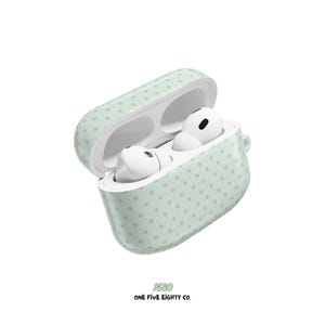 May include: An open mint green case with pink polka dots, holding white wireless earbuds. The case has a matching polka dot pattern. The text "1580" and "ONE FIVE EIGHTY CO." are printed at the bottom.