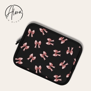Könnte beinhalten: Schwarze Laptoptasche mit einem Muster aus rosa Schleifen. Die Tasche hat einen Reißverschluss.