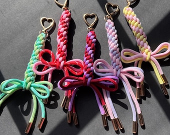 Puede incluir: Cinco llaveros coloridos con cierres en forma de corazón. Cada llavero presenta un cordón trenzado en una combinación de colores diferente: verde y rosa, rojo y rosa, rojo y morado, morado y rosa, y amarillo y rosa. Cada uno tiene un lazo y detalles metálicos dorados.
