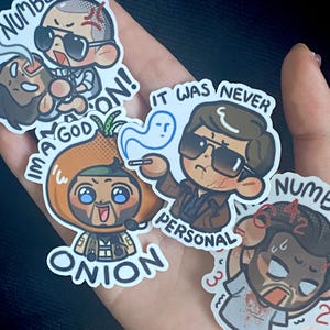 May include: Five colorful stickers featuring cartoon characters with different expressions and text. The stickers include the text "Numbers", "I'm a God", "It was never personal", "Onion", and "Numbers".