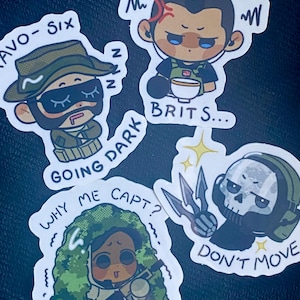 Puede incluir: Cinco pegatinas de dibujos animados con personajes del videojuego Rainbow Six Siege. Las pegatinas están impresas sobre un fondo blanco. La primera pegatina presenta un personaje con un sombrero verde y el texto "AVO-SIX GOING DARK". La segunda pegatina presenta un personaje con un sombrero negro y el texto "BRIT S...". La tercera pegatina presenta un personaje con un sombrero verde y el texto "WHY ME CAPT?". La cuarta pegatina presenta un personaje con un casco negro y el texto "DON'T MOVE". La quinta pegatina presenta un personaje con un sombrero verde y el texto "~Z".
