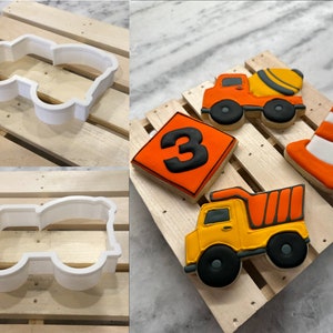 Puede incluir: Un conjunto de cinco galletas de azúcar con temática de construcción. Las galletas están decoradas con glaseado naranja, amarillo, negro y blanco. Las galletas incluyen una mezcladora de cemento, un camión volquete, un cono, un número tres y un cortador de galletas para un camión volquete.