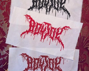 May include: Three fabric patches with the word "BODHI" in a gothic font. The top patch has black text, the middle patch has red text, and the bottom patch has red text. The patches are on a patterned red and gold background.