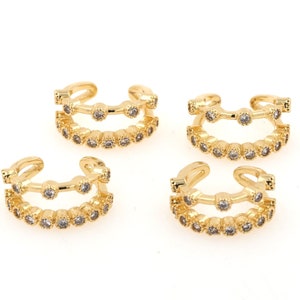 Può includere: Quattro orecchini a cerchio dorati con strass trasparenti. Ogni orecchino ha due file di strass.