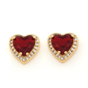 May include: A pair of gold heart-shaped earrings with red cubic zirconia stones and a halo of smaller white cubic zirconia stones.