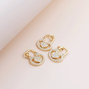 May include: Three gold-tone padlock charms with clear crystal embellishments. Each charm features a heart-shaped design.