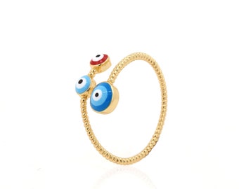 Puede incluir: Un anillo de oro con tres amuletos de ojo turco azul y blanco. El anillo está retorcido y tiene una superficie texturizada.