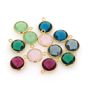 May include: Assortment of 10 round glass charms with gold-toned metal settings. The charms feature various colours including pink, green, blue, and purple.