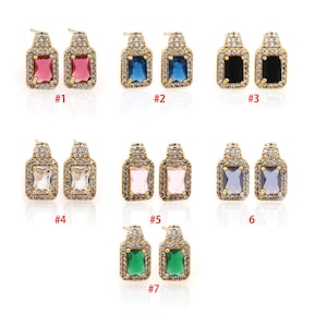 May include: Seven pairs of gold earrings with different colored gemstones. Each pair features a square-shaped gemstone surrounded by a halo of smaller clear stones. The gemstones are red, blue, black, clear, pink, purple, and green.