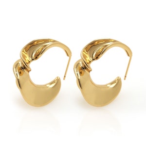May include: A pair of gold hoop earrings with a unique, organic shape. The earrings are made of a smooth, polished metal and have a modern, minimalist design.