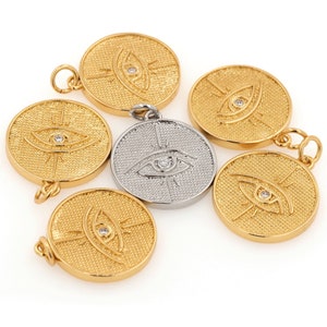 May include: Six gold and silver pendants with a raised eye design and a small clear rhinestone in the center. The pendants are round and have a textured surface.