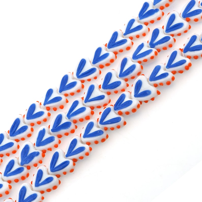May include: A strand of white heart-shaped beads with blue and orange accents. The beads are strung together to create a necklace or bracelet.