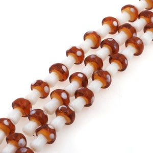 May include: A strand of brown and white glass beads shaped like mushrooms with white polka dots.