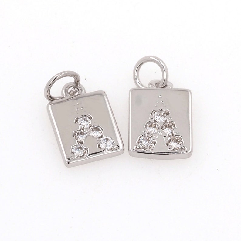 Peut inclure: Deux breloques argent&eacute;es en forme de carr&eacute;s avec une lettre A en strass transparent au centre. Les breloques ont une boucle en haut pour s'attacher &agrave; un bracelet ou un collier.
