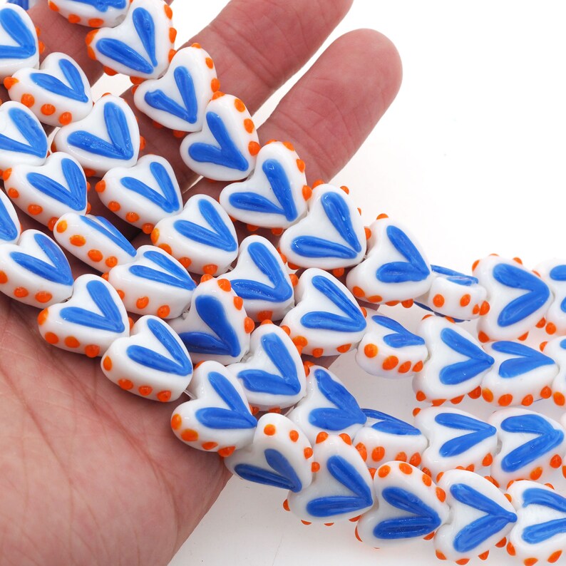 May include: A strand of white heart-shaped glass beads with blue and orange accents. The beads have a textured surface and are strung together on a clear thread.