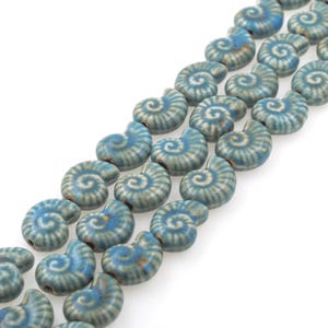 Könnte beinhalten: Eine Strähne blauer Keramikperlen in Form von Muscheln. Jede Perle hat ein weißes Spiralmuster.