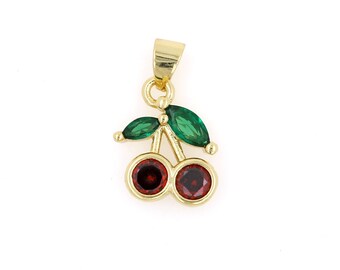 May include: A gold-colored cherry pendant with red and green gemstones. The pendant features two red cherry stones and green leaf accents. The pendant is designed to be worn as a necklace.