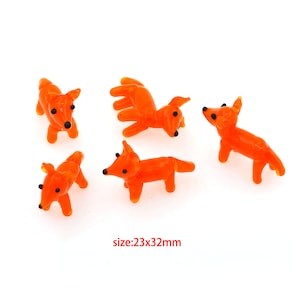 Puede incluir: Cinco figuritas de zorro de vidrio naranja, cada una de aproximadamente 5,8 cm por 8,1 cm. Los zorros están en varias poses, algunos de pie y otros sentados.