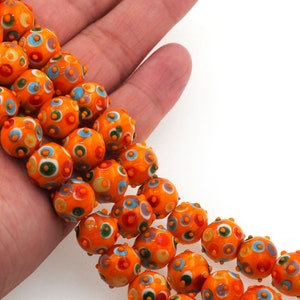 May include: A strand of orange glass beads with colorful polka dots. The beads are round and have a textured surface.