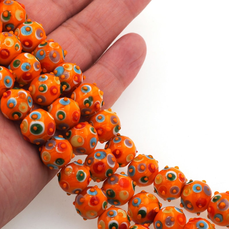 May include: A strand of orange glass beads with colorful polka dots. The beads are round and have a textured surface.