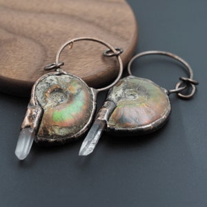 Peut inclure: Une paire de boucles d'oreilles avec des fossiles d'ammonites irisées et des cristaux de quartz transparents attachés à des cercles en cuivre.