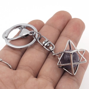 Könnte beinhalten: Silberner Schlüsselanhänger mit einem violetten Amethyststein in einem sternförmigen Käfig aus Silber.