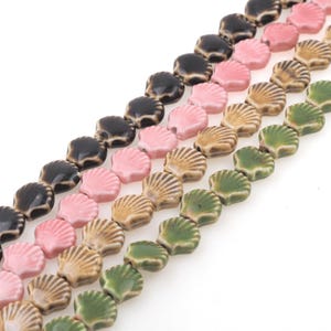 Könnte beinhalten: Eine Schnur aus Keramikperlen in Form von Muscheln. Die Perlen sind in vier Farben: grün, braun, rosa und schwarz.
