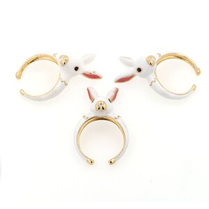 May include: Three gold-tone rings with white enamel bunny rabbit designs. The bunnies have pink ears and black eyes.