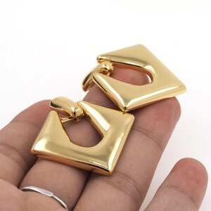 May include: A pair of gold-tone geometric earrings with a square shape and a hollow center.