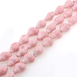 May include: A strand of pink ceramic beads in a teardrop shape. The beads have a textured surface and are strung on a clear thread.