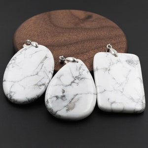 May include: Three white howlite pendant charms with silver bail loops. The charms are in the shape of a teardrop, oval, and rectangle.