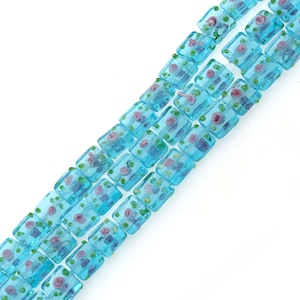 May include: Rows of rectangular, light blue glass beads with floral designs. Each bead features pink roses, green dots, and other floral elements. The beads are strung together, creating a decorative pattern.