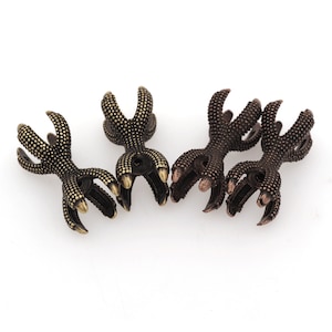 Puede incluir: Cuatro piezas decorativas en forma de garra de metal dorado antiguo. Las garras están detalladas con pequeños puntos en relieve y tienen un agujero en el centro.