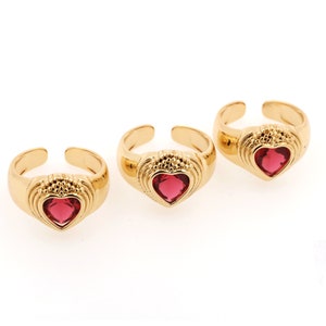 May include: Three gold rings with a heart-shaped red gemstone in the center of each ring.
