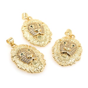 May include: Three gold lion head pendants with clear and green rhinestones. The pendants are oval shaped and have a detailed design.