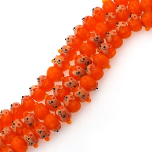 May include: A strand of orange glass beads with a cartoon face design. Each bead has a smiling face with black eyes and a red mouth.