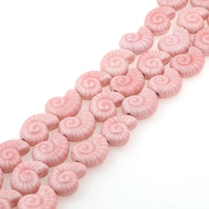Puede incluir: Una hebra de cuentas de cerámica rosa con forma de conchas marinas. Cada cuenta tiene un patrón en espiral detallado.