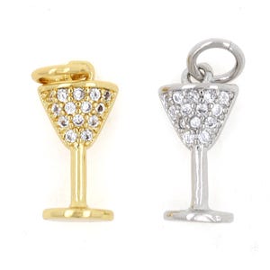 Puede incluir: Dos colgantes con forma de copa de martini, uno dorado y otro plateado, ambos con detalles de cristal transparente.