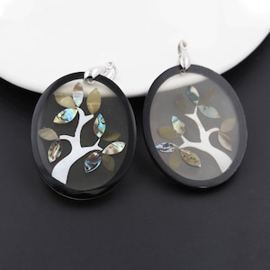 May include: Two round black and silver pendant earrings with a white tree design and iridescent abalone shell leaves.