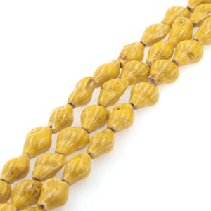 Può includere: Una collana di perline in ceramica gialla con una superficie testurizzata leggermente ruvida. Le perline hanno la forma di lacrime allungate.